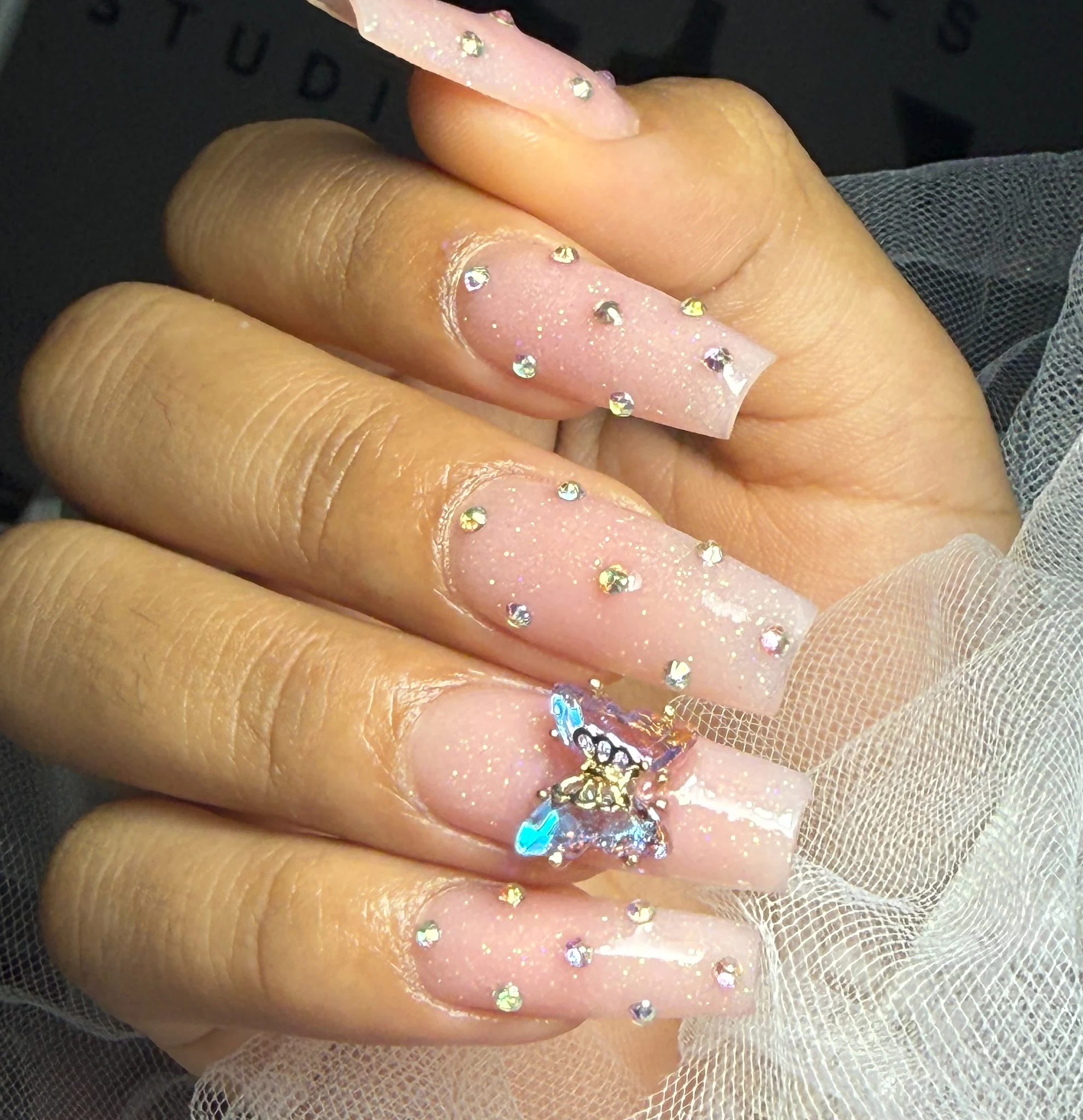 Uñas rosadas con cristales y adorno de mariposa